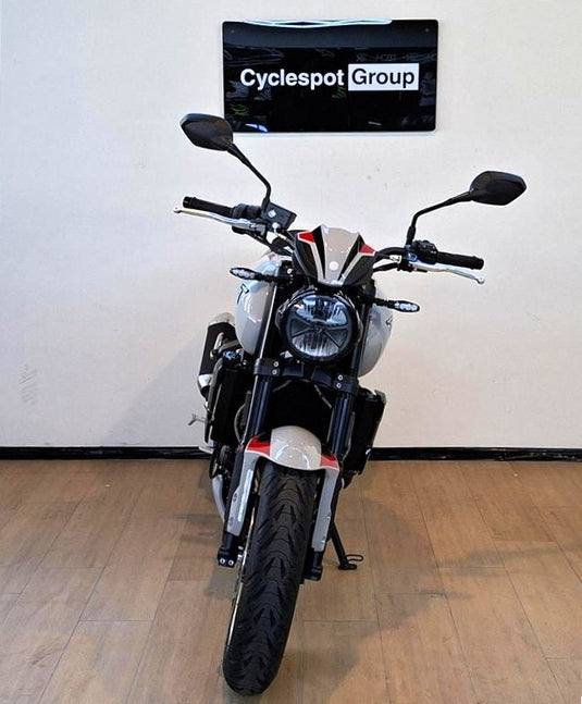 A black and silver Triumph Trident cruiser motorcycle with red accents, photographed from the front in a showroom with a wood floor and a wall sign reading 'Cyclespot Group'.