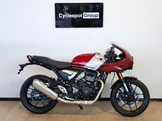 A side view of a 2026 Triumph Thruxton 400 in Carnival Red on a wooden floor, backed by a white wall with a Cyclespot Group sign in white on black.