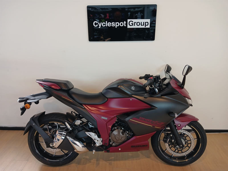 Load image into Gallery viewer, Crimson red and black 2025 Suzuki GSX 250 FR motorcycle on display with 'Cyclespot Group' branding in the background
