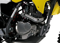 Close-up of a motorcycle engine and exhaust system, showing a silver engine block, black exhaust pipe, and yellow body panel on a white background.